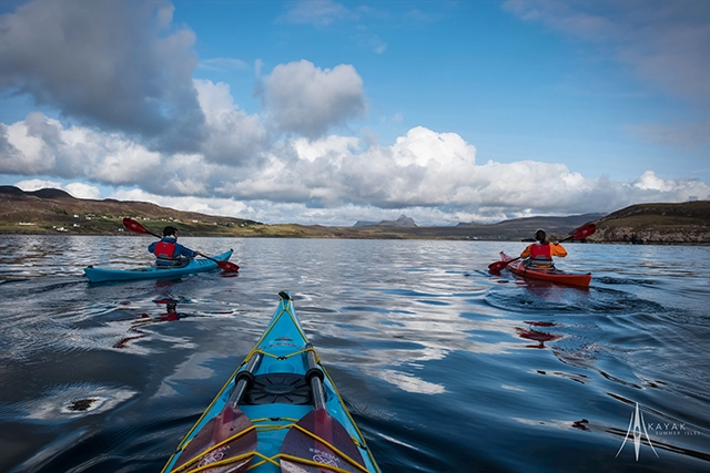 Kayak Summer Isles out on the sea with customers. 3 kayaks paddle along calm water between the Summer Isles and Ullapool on a nice day