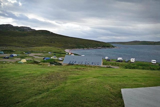 A view of Port a Bhaigh campsite near Achiltibuie, 1 hour north of Ullapool. Shows green grass, some camping spots and caravan hookups by the beach